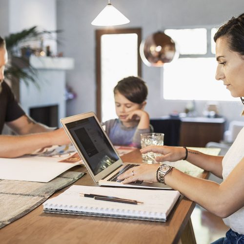 Kvinna jobbar hemma med bärbar dator och familj i bakgrunden